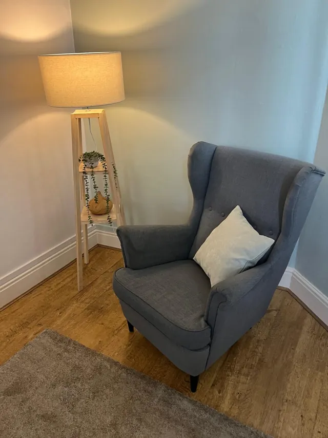Grey wingback chair with a pale cushion beside a lit wooden floor lamp