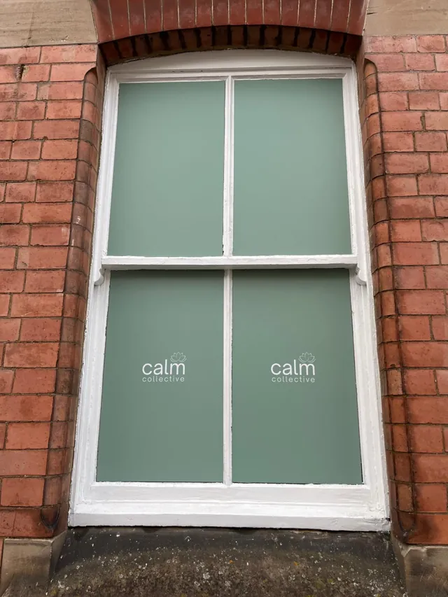 Calm Collective logos on sage window film framed by red brick