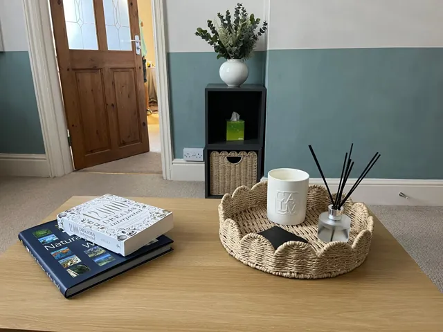 Books, a woven tray, candle and diffuser on a wooden coffee table