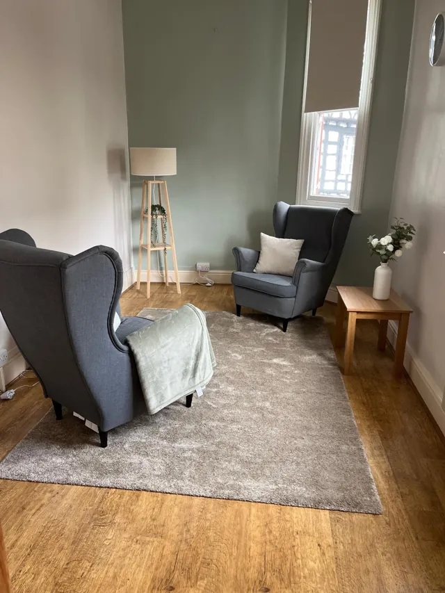 Two grey armchairs, a soft rug and a sage feature wall in a Calm Collective therapy room