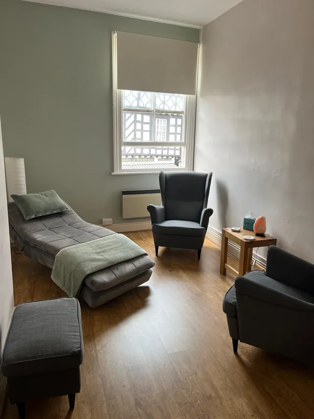 Therapy room with a reclining couch, grey chairs and a sash window